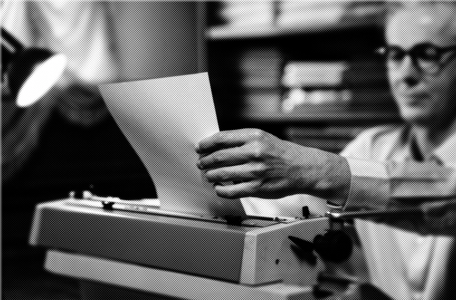 A dark, distorted, halftone image of a man in glasses lifting a sheet of paper from a typewriter.