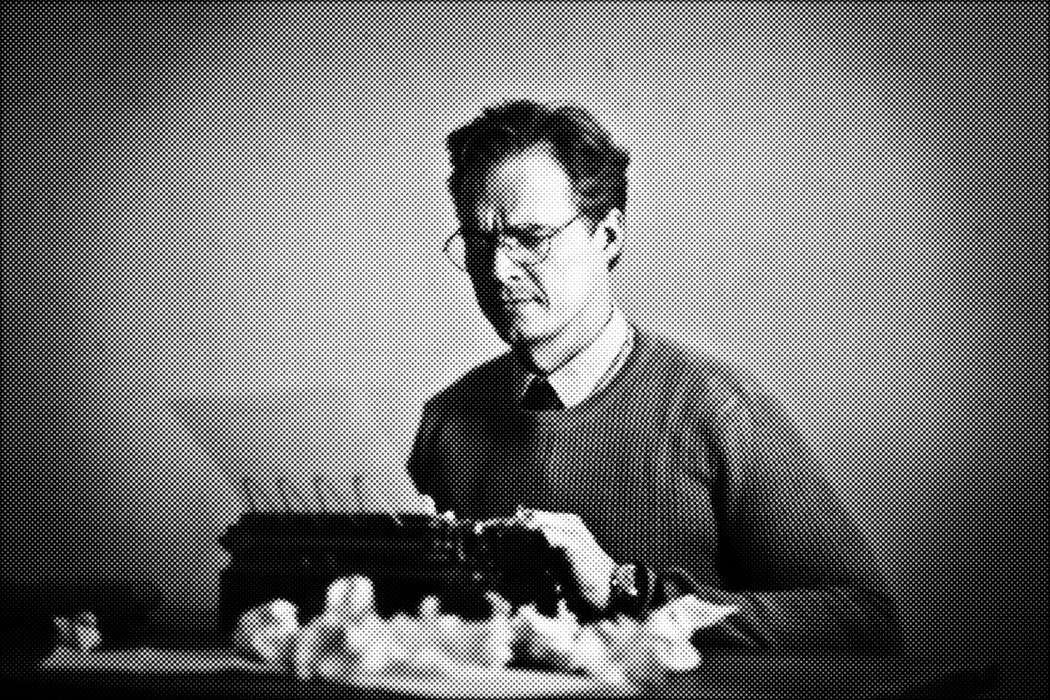 A dark, distorted, halftone image of a man in glasses sitting confused in front of a typewriter with several crumpled balls of paper.