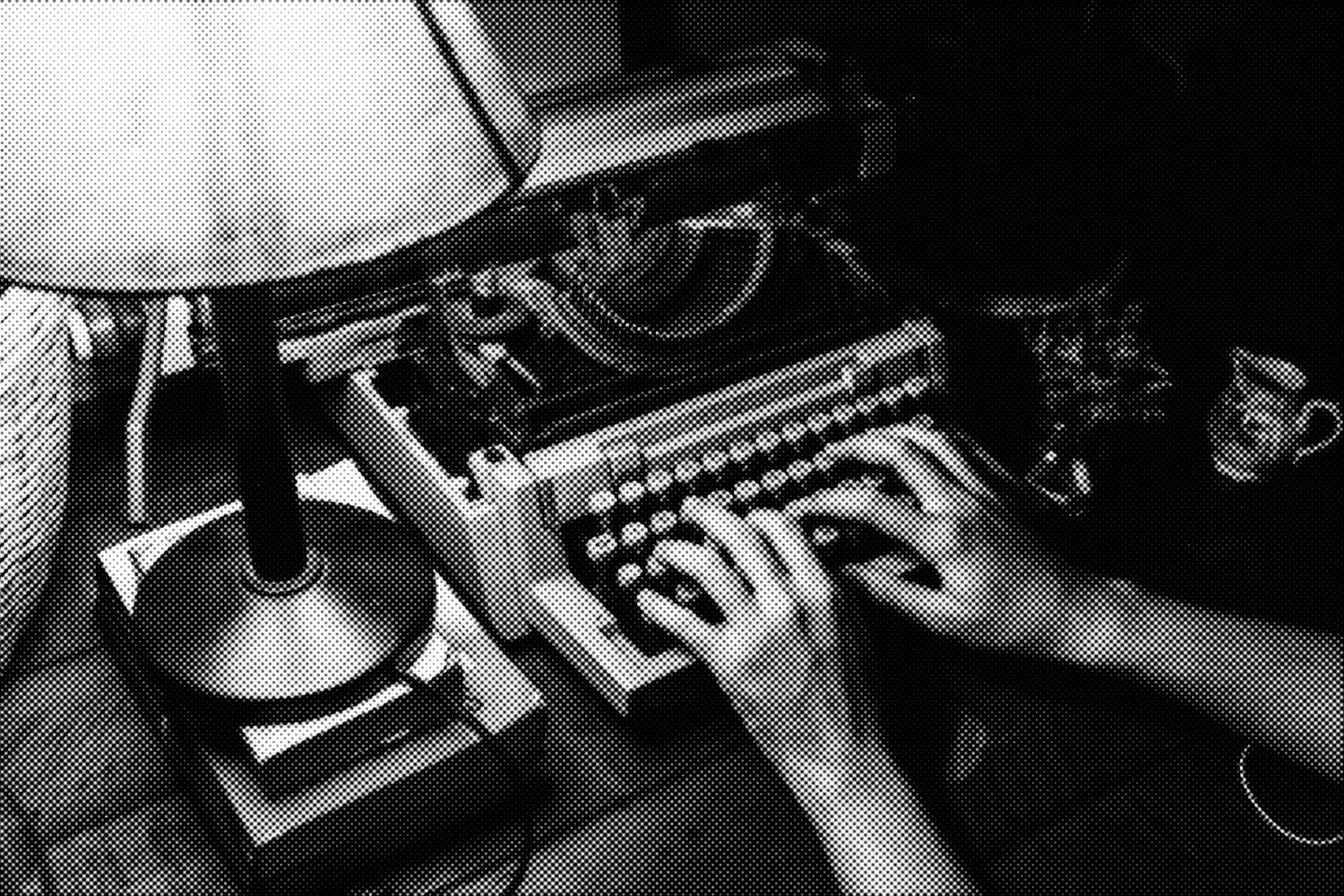 A dark, distorted, halftone image of a person typing on a typewriter under the light of a prominent shaded lamp.